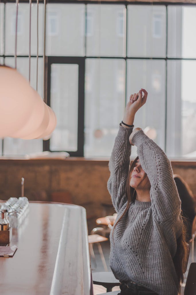 Woman stretches in a cozy cafe, enjoying a relaxed moment by the window.
